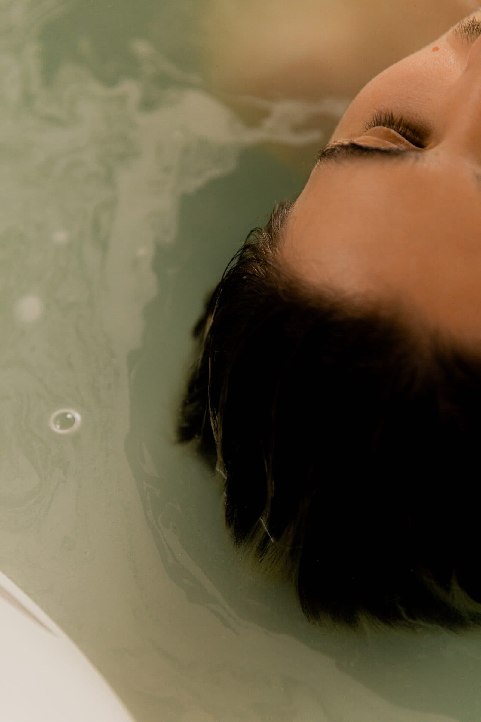A woman resting back in a warm bath with her eyes closed