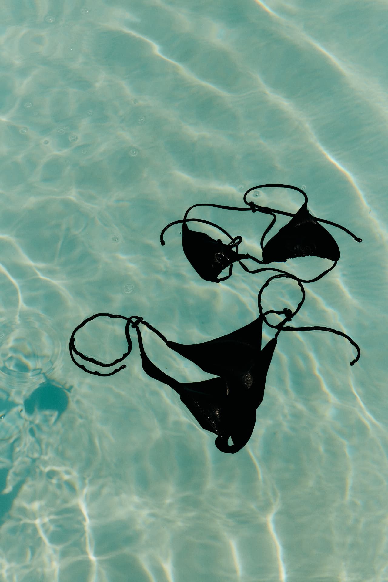 A black bikini floating in clear, sunlit water