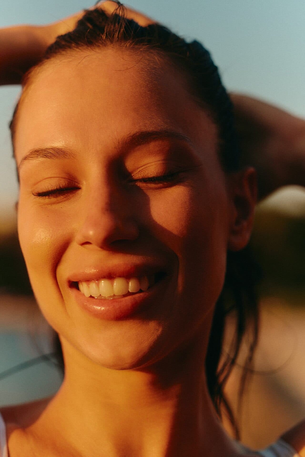 A smiling woman with her eyes closed, her face warm in the late sun