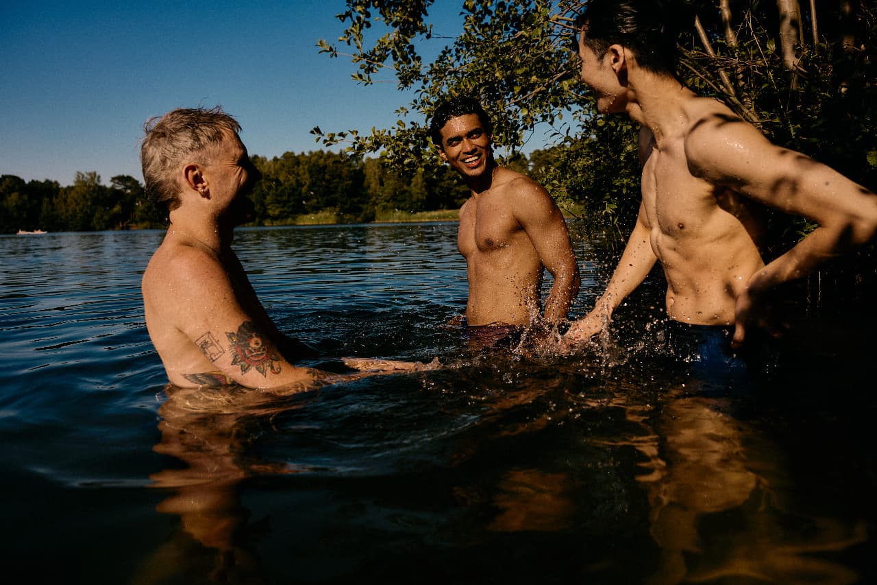 Three men laughing together waist-deep in a river on a sunny day