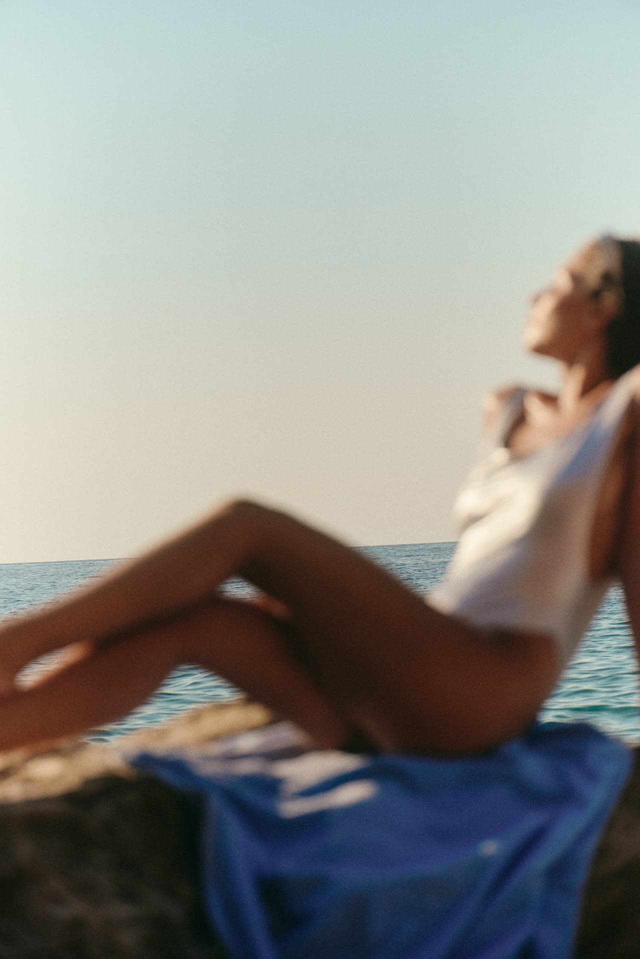 A softly focused figure resting beside the sea
