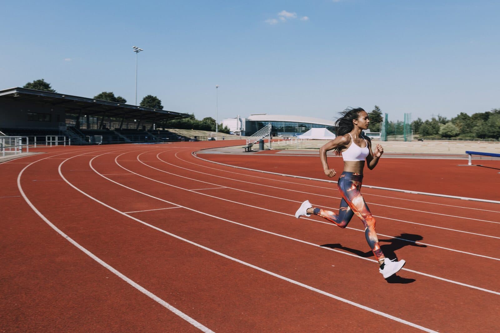 A woman sprinting along a red running track on a clear day