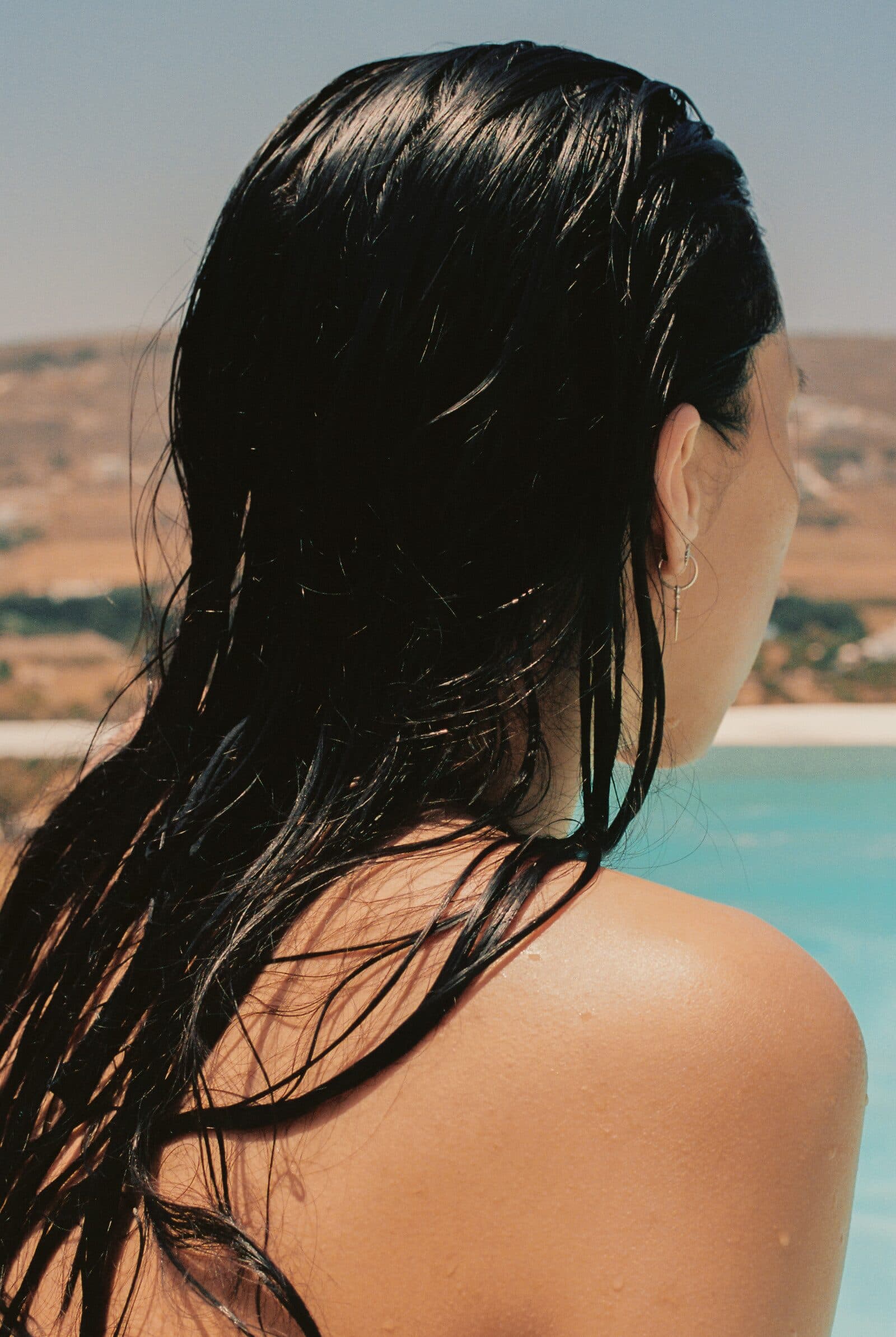 A woman with long, wet dark hair looking out over a turquoise pool
